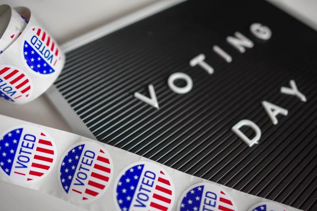 a roll of voting stickers lay on a voting day sign to symbolize the fact that cybersecurity professionals protect US election from cyberattacks