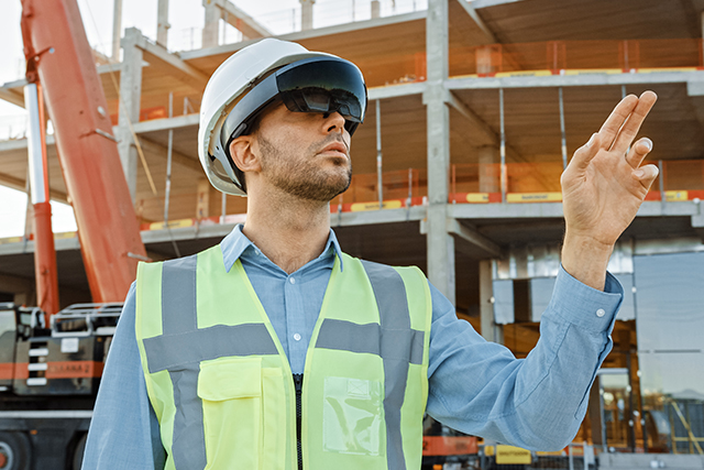 a man in a hard hat with VR googles uses virtual and augmented reality technology in construction management