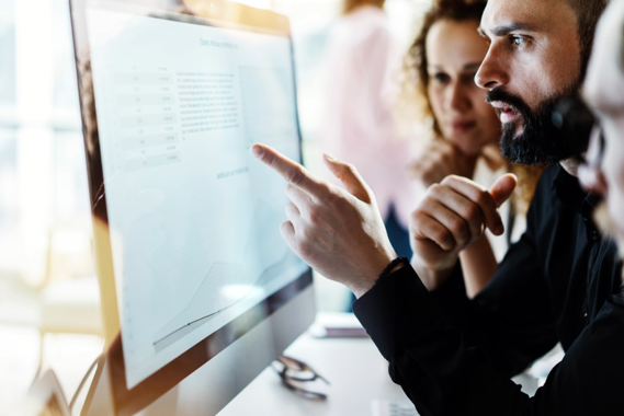 Stock photo of a man pointing to a screen while colleagues watch.