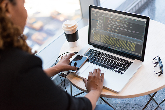 a woman in a cafe works on identity based application security for networks on her laptop