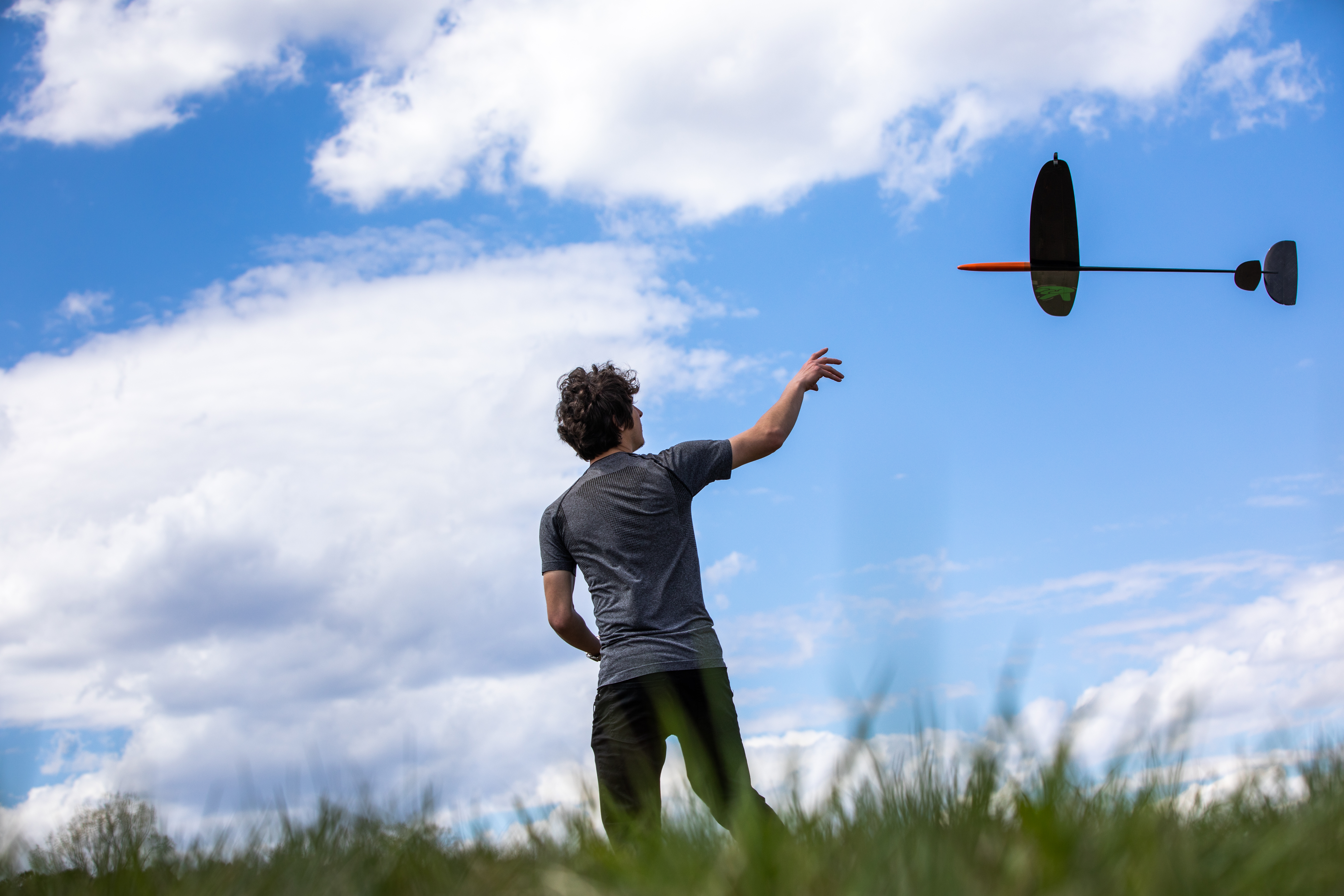 student in field reaching toward model airplane
