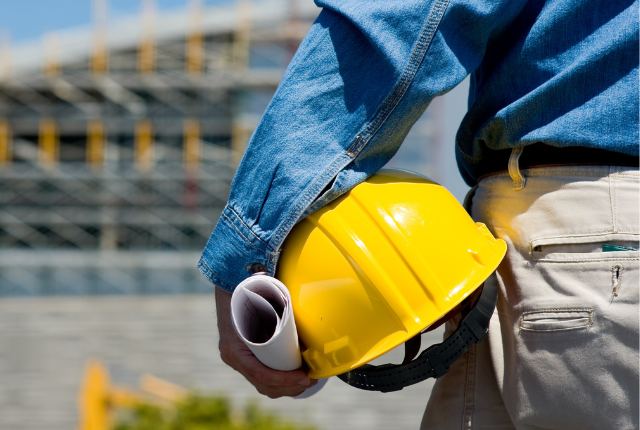 close up of construction worker's arms holding hard hat and blueprint 
