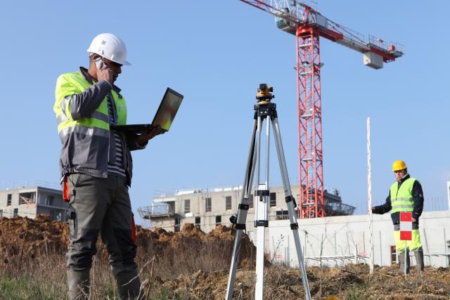 A construction worker talking on phone while looking at laptop at the construction site