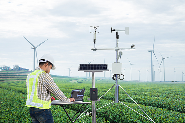 a man in a hard hat works on a computer in a wind turbine field forecasting wind patterns using machine learning