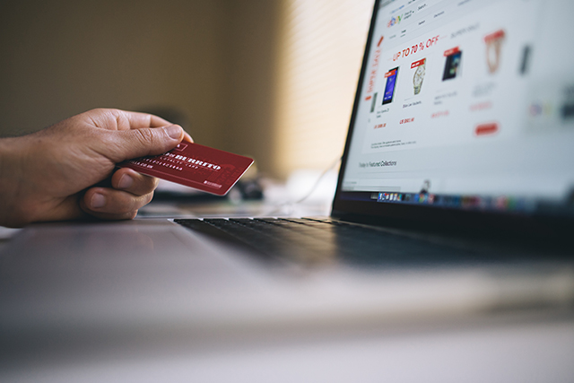 a consumer holds their credit card next to an open laptop to symbolize how e-commerce retailers are managing cybersecurity