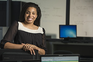 a portrait of Capitol Tech Cybersecurity alum Kierra Jiles seated in front of a computer at her cybersecurity career