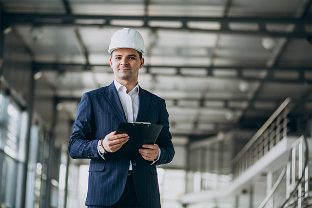 a man in a suit and hard hat stands with a clipboard demonstrating the value of a construction management degree for veterans