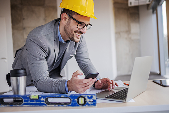 man in business suit and hard hat looking at laptop