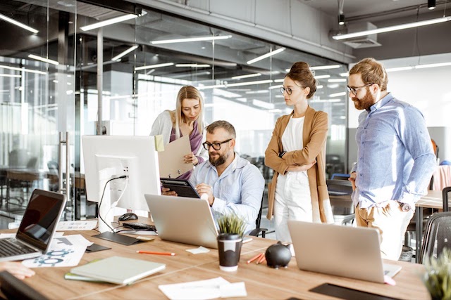 A group of men and women at computers discuss cyber attacks on their small company