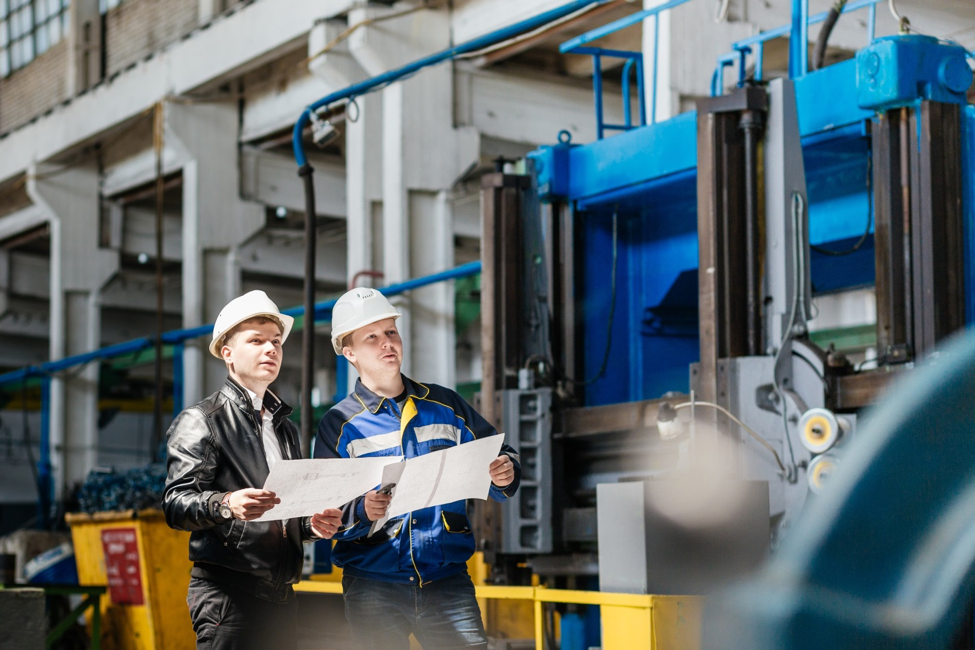 Two men in hard hats studying plans on construction site for manufacturing plant