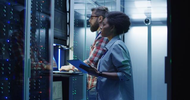 Man and woman in server room looking at laptop showing cybersecurity jobs in private sector