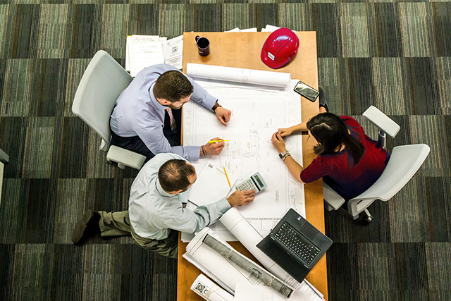 an overhead shot of two men and a woman collaborating around blueprints symbolizes the fastest growing careers in construction industry