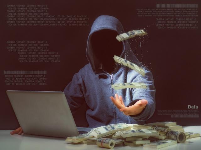 Faceless person sitting in front of laptop with money symbolizing ransomware in cybersecurity