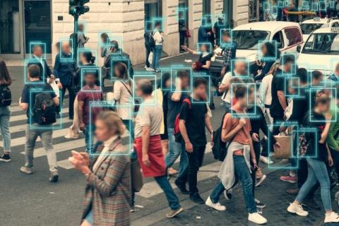 a large group of people walk through an intersection while their faces are being recognized to demonstrate the use of ai in social cognition