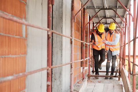 one construction worker helps another on some scaffolding demonstrating construction safety ergonomics