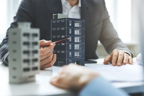 a man in a suit points to a model of a building in a meeting to demonstrate that construction bidding activity is on the rise