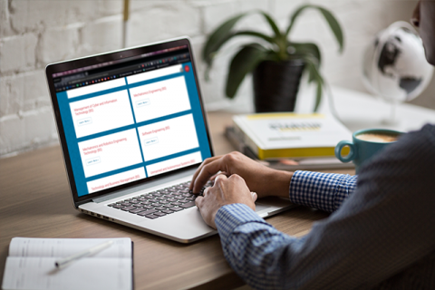 a person sitting at a desk looking at the Capitol Tech University Bachelor’s degree page to find the mechatronics robotics engineering program