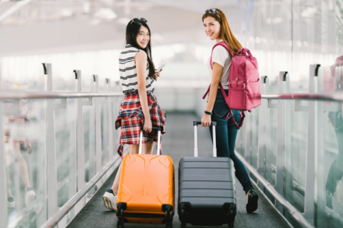 two women on moving walkway with rolling suitcases