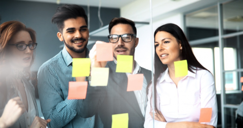 group of people writing out information on post-its on a glass wall