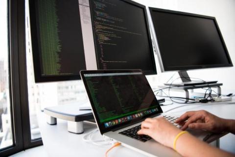 a person is on a laptop surrounded by screens to symbolize data analytics, machine learning and AI in healthcare industry